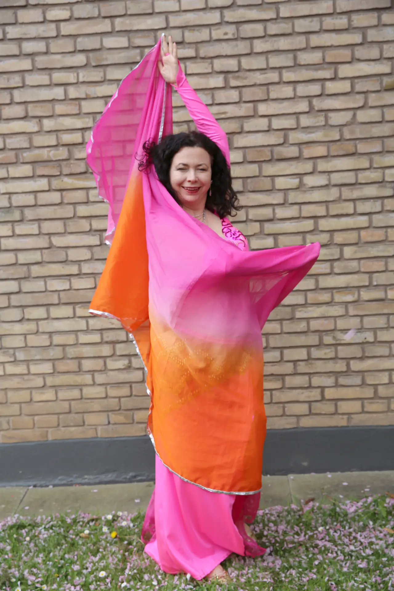 Mavedanser i fuld figur med front mod fotografen, sløret ført foran kroppen og bagom op i venstre hånd, mens højre arm dækker for barmen.