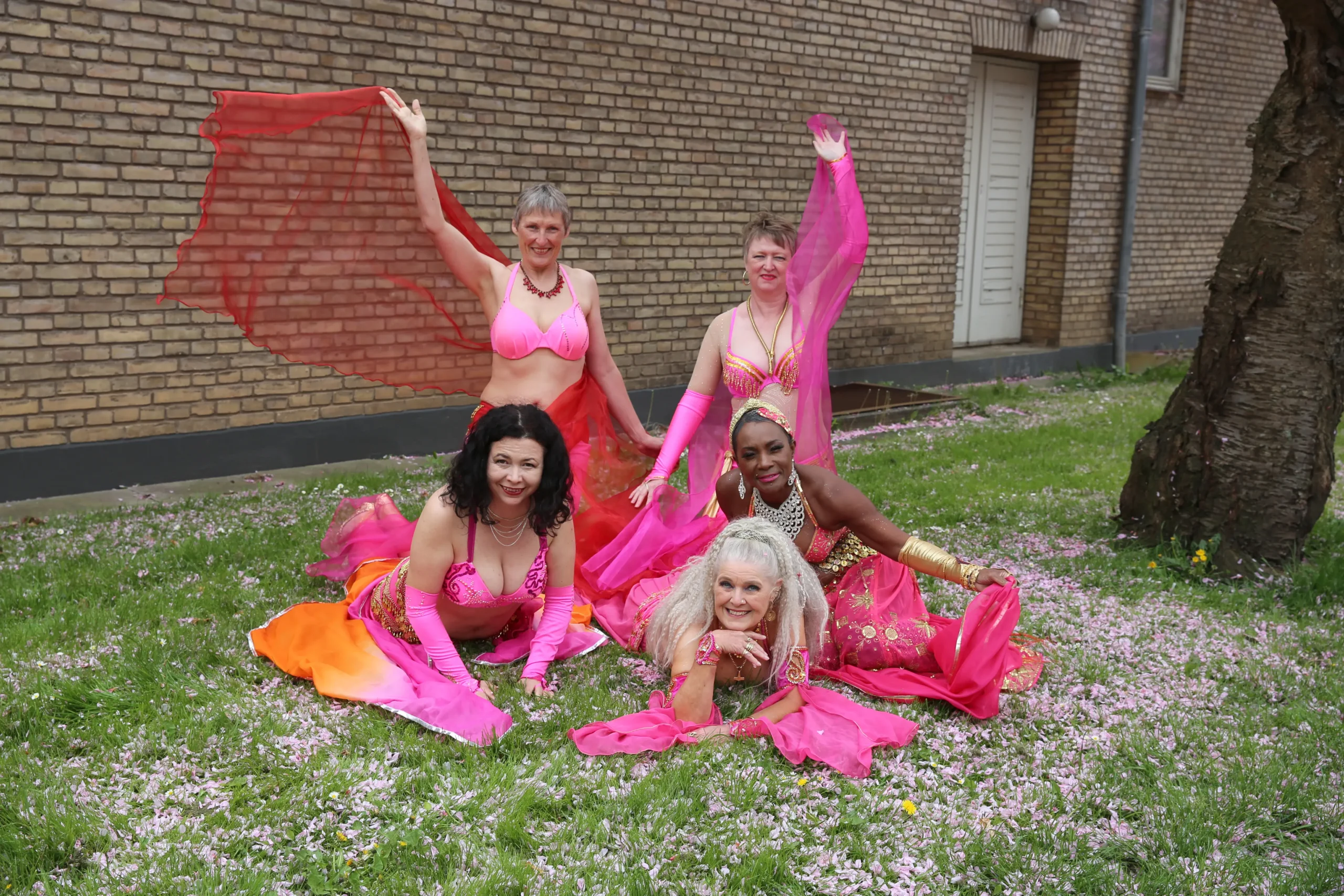 Dansere i pink kostumer ligger legende på Aziza i kirsebærblomster under træ