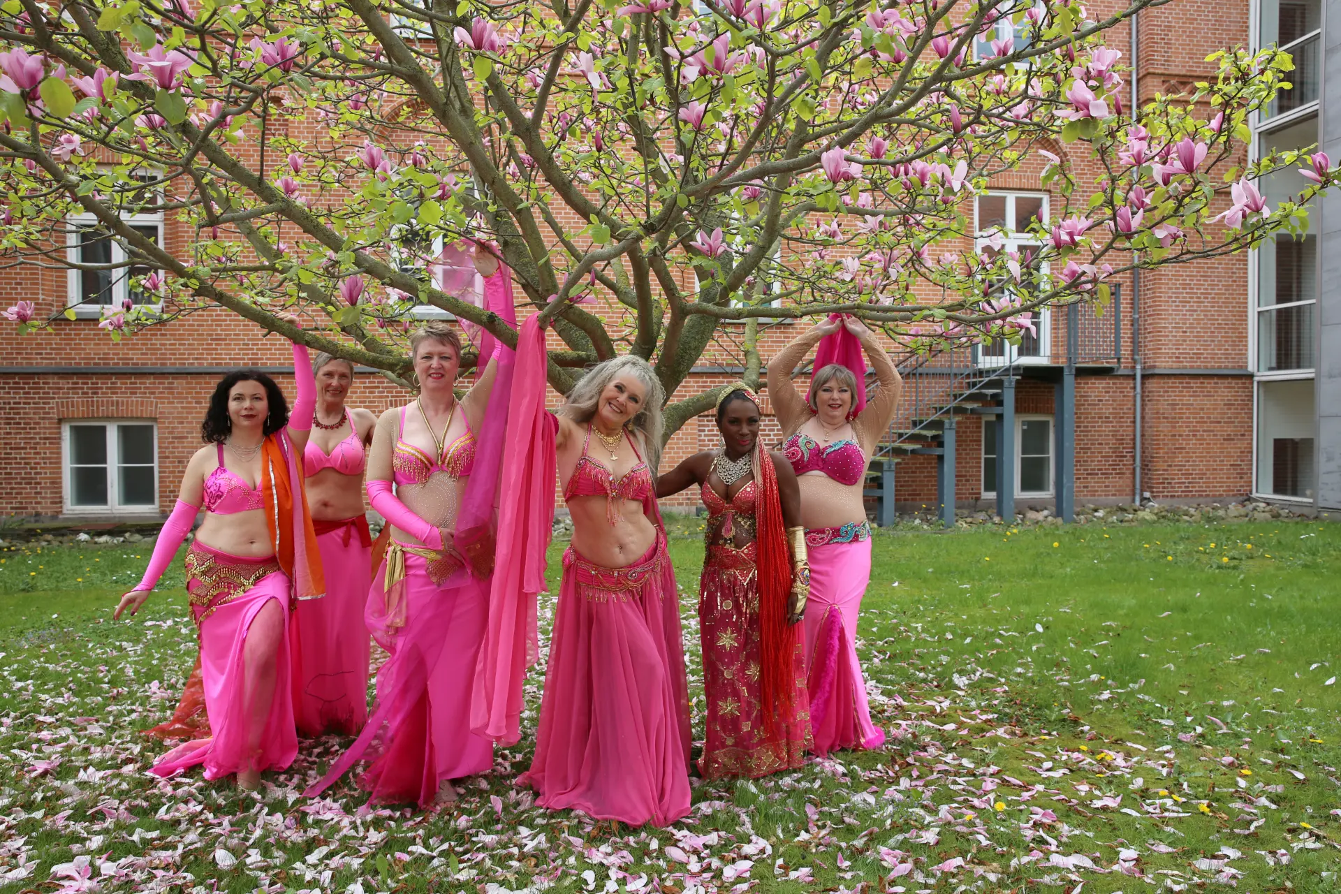 Gruppebillede under magnoliatræet med danserne stående på græsset blandt nedfaldne kronblade.