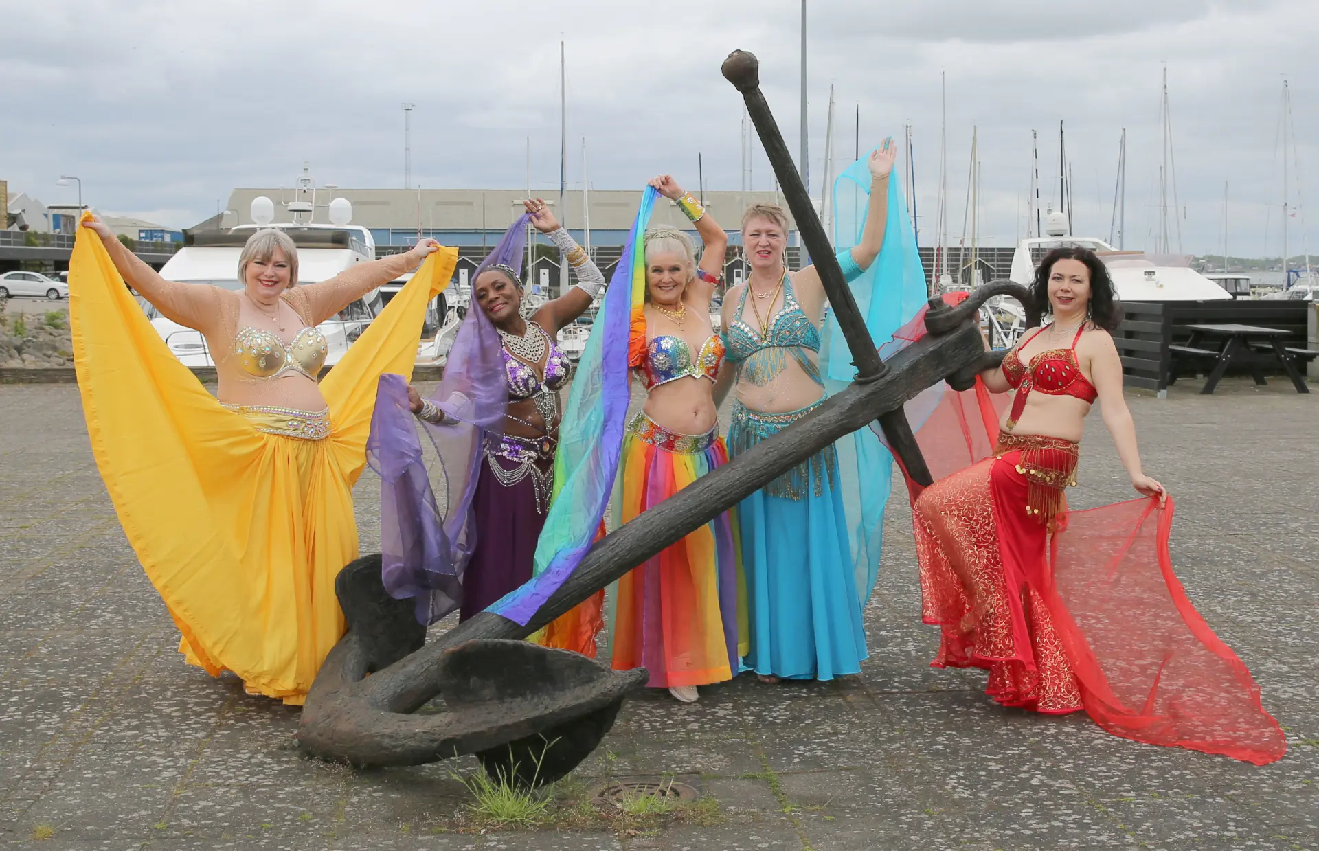 Gruppebillede fra Mavedans Danmarks Fotosession 2025 ved lystbådehavnen med danserne foran det store anker.