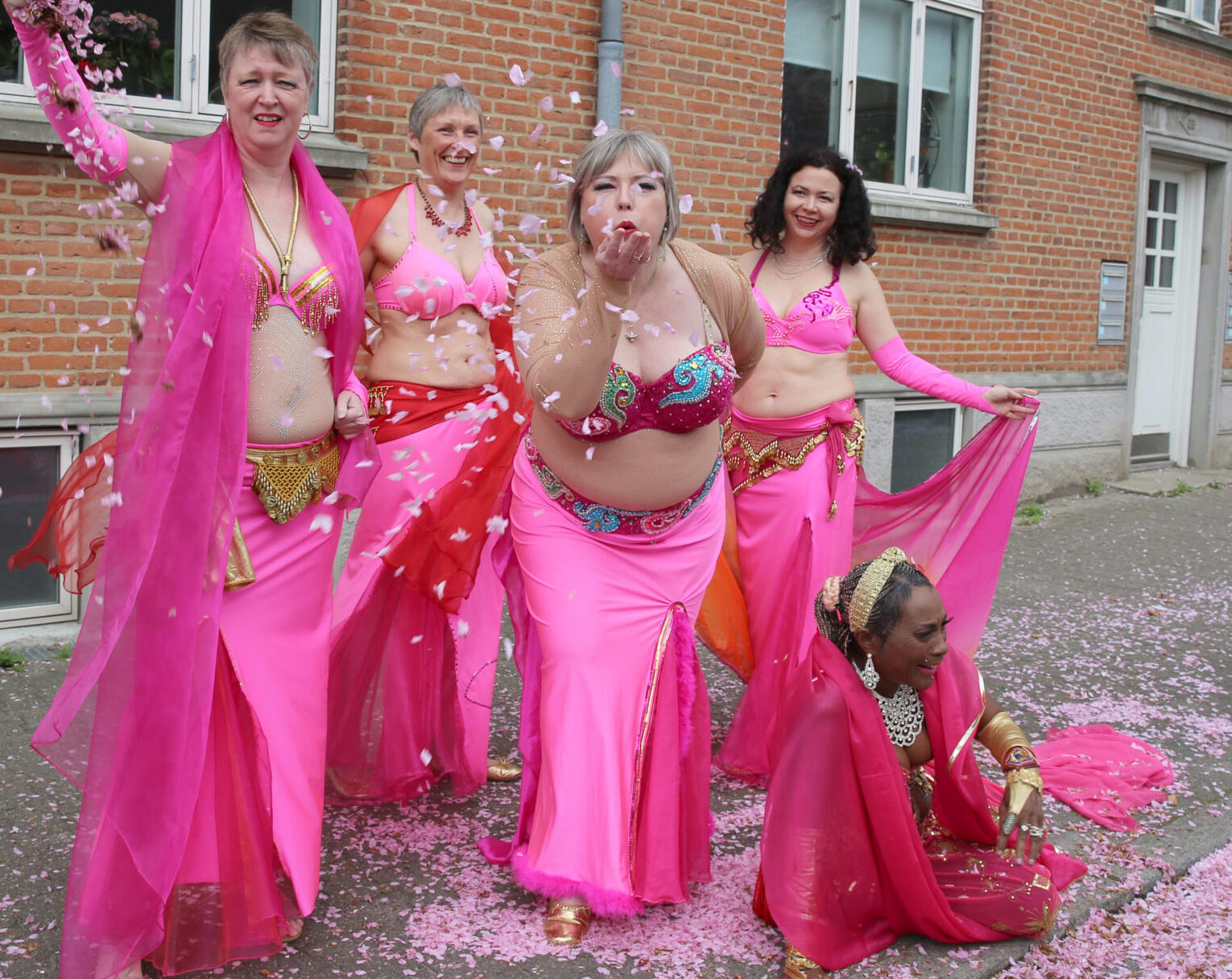 en flok mavedansere i pink kaster rundt med pink kirstbærblomster midt på gaden