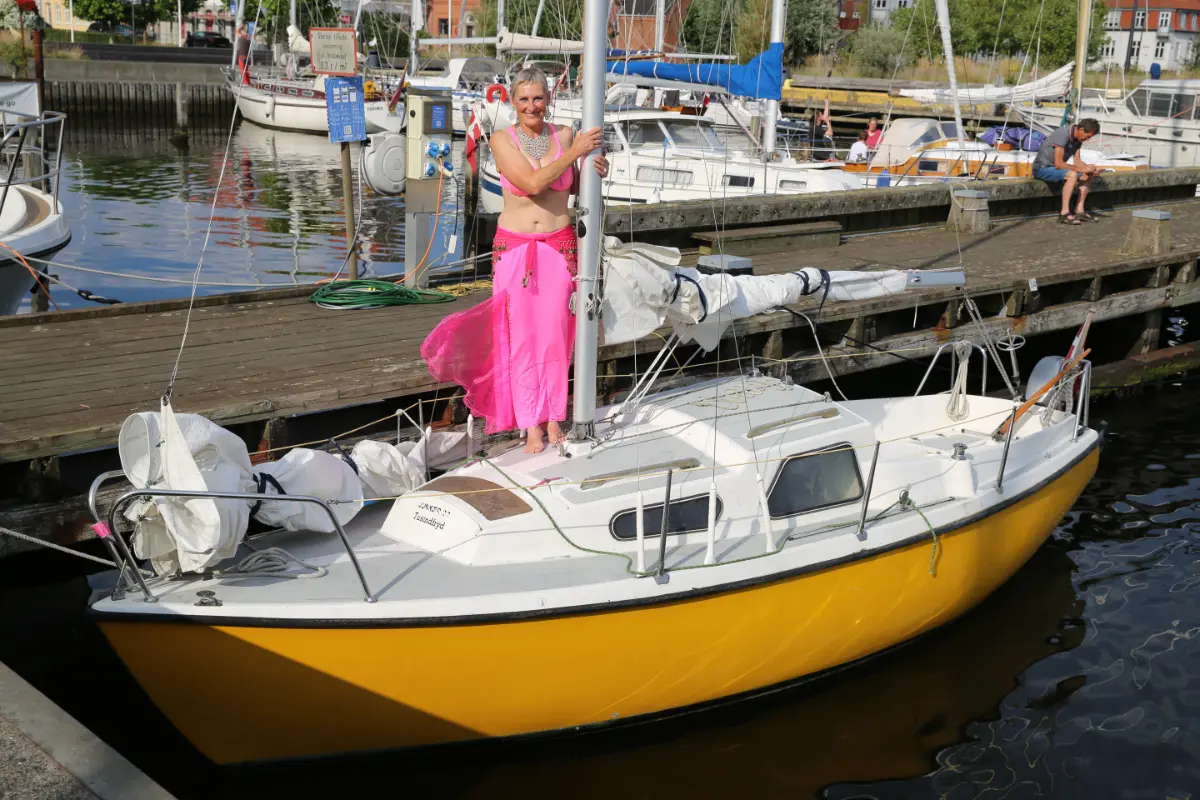 Mavedanser i fuld kostume står på sin lille sejlbåd der ligger i havn