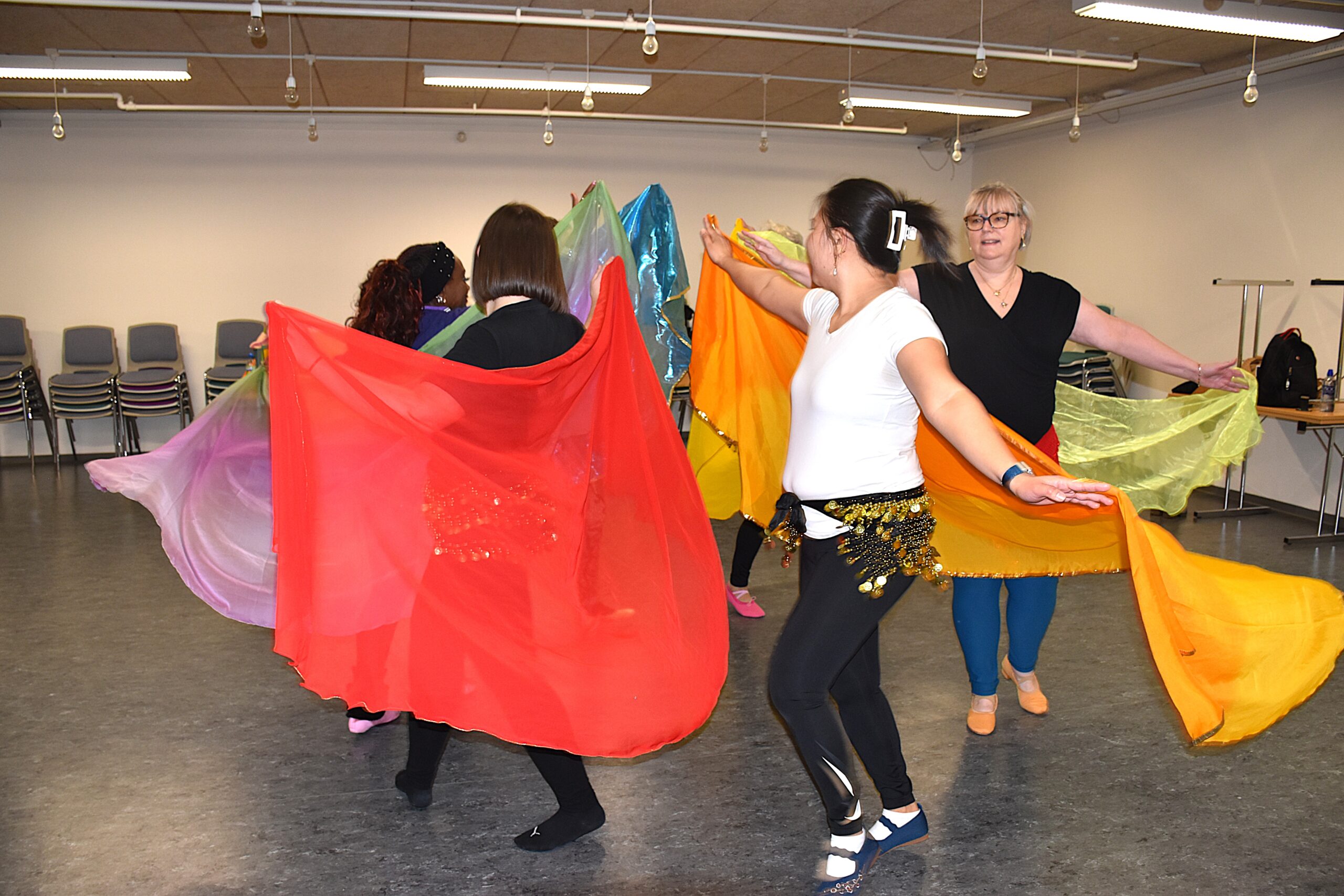 En gruppe mavedansere træner, de danser rundt i en cirkel med slør